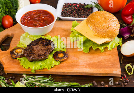 Stillleben mit gegrillten Hamburger und Pilze auf Holzbrett umgeben von frischem Gemüse und Belag auf rustikalen Holztisch hautnah. Stockfoto