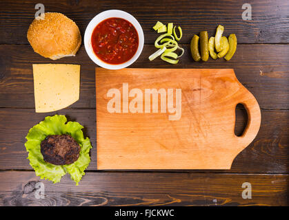 High Angle View of zerlegten Hamburger mit Käse und frischen Belägen auf rustikalen Holztisch liegend mit abgenutzten Schneidebrett und Textfreiraum. Stockfoto