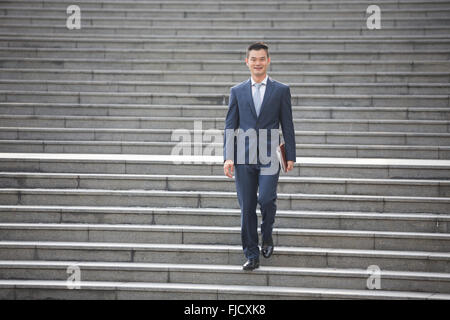 Porträt eines glücklichen asiatischen Geschäftsmann Treppen hinunter. Chinesischer Geschäftsmann walking im Freien. Stockfoto