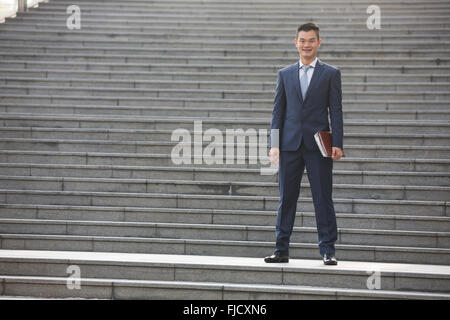 Porträt eines glücklichen asiatischen Geschäftsmann Treppen hinunter. Chinesischer Geschäftsmann walking im Freien. Stockfoto