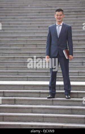 Porträt eines glücklichen asiatischen Geschäftsmann Treppen hinunter. Chinesischer Geschäftsmann walking im Freien. Stockfoto