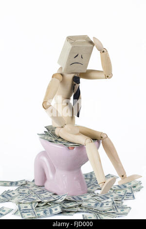 Ein deprimierter Geschäftsmann aus Holz, der auf einer Toilettenschüssel mit Bargeld sitzt. US-Finanzkrise und bärisches US-Dollar-Konzept. Stockfoto