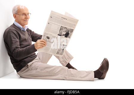 Fröhlichen senior Gentleman auf dem Boden isoliert auf weißem Hintergrund sitzende Zeitung lesen Stockfoto