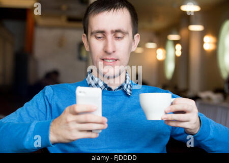 Porträt von lässig entspannt lächelnd junger Mann im modernen Café drinnen sitzen, Handy halten, mittels Smartphone telefonieren Stockfoto