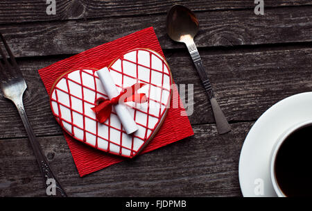 Schöne rote herzförmige gestreiften Cookie mit einer Überraschung Notiz auf rustikalen Holz. Valentinstag-Frühstück-Konzept. Stockfoto