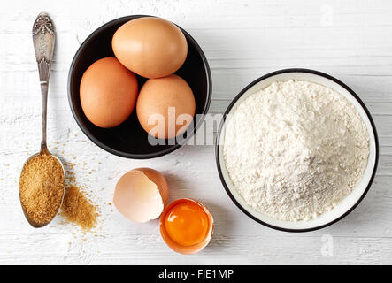 Backen, Eiern, weißes Mehl und Zucker auf weißer Holztisch, Ansicht von oben Stockfoto