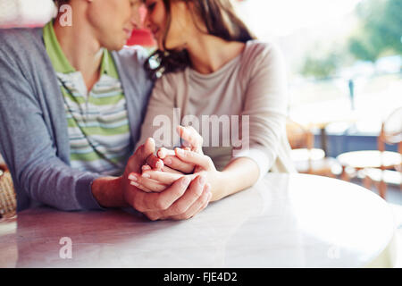 Junges Paar sitzt am Tisch und Hand in Hand Stockfoto