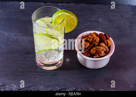 Gin und Tonic mit Kalk, garniert mit Schale nach Hause gerösteten Nüssen serviert. Stockfoto