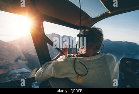 Heckansicht des weiblichen Touristen auf Hubschraubertour fotografieren während des Fluges über Berge an einem sonnigen Tag. Stockfoto