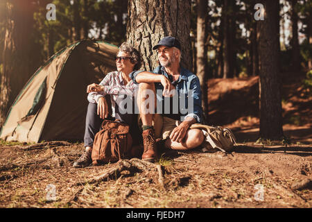 Porträt von älteres paar beisammen sitzen unter einem Baum im Wald und mit Blick auf einen Blick. Reifer Mann und Frau entspannen in ihrer Stockfoto