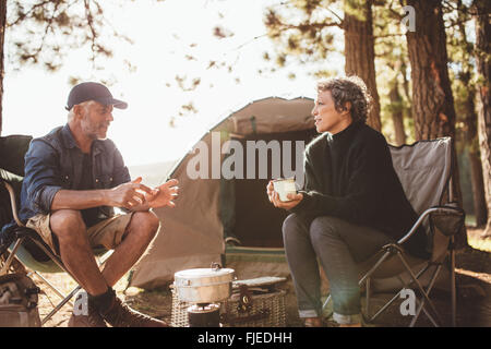 Reifer Mann und Frau sitzen und reden auf einem Campingplatz. Älteres paar sitzen auf Stühlen außerhalb des Zeltes an einem Sommertag. Stockfoto