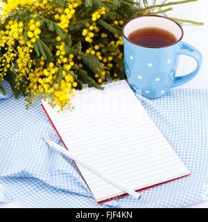 Mimosen Blüten, Notizblock und Tasse Tee auf einem blauen Tuch, Stockfoto