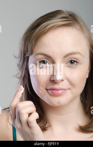 Attraktive junge Frau, die feuchtigkeitsspendende Creme auf ihr Gesicht auftragen Stockfoto
