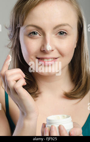 Attraktive junge Frau, die feuchtigkeitsspendende Creme auf ihr Gesicht auftragen Stockfoto