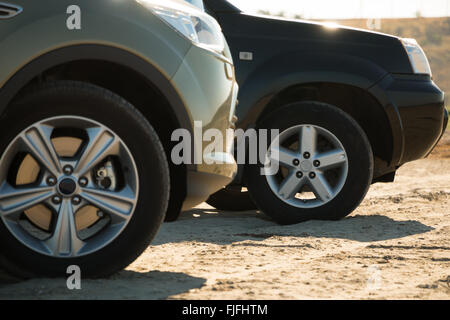 Sonniger Tag. Sand und Rasen im Hintergrund. Zwei SUVs sind. Vorderräder sind hautnah Stockfoto