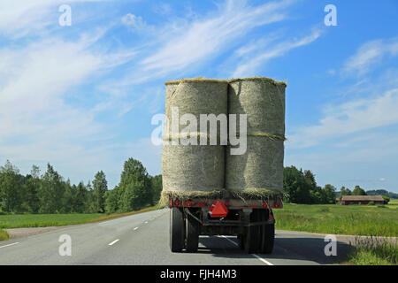 Traktor Transport Heuballen auf landwirtschaftliche Anhänger auf Autobahn im Sommer. Stockfoto