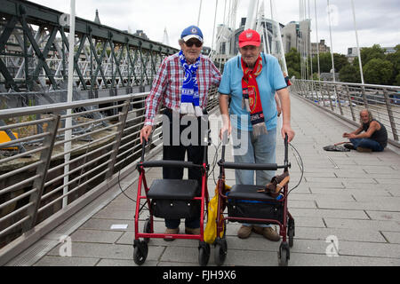 Zwillingsbrüder, die Unterstützung gegen Fußball teams gehen gemeinsam über die Golden Jubillee Bridge neben Hungerford Bridge. Der Bruder auf der linken Seite unterstützt FC Chelsea und seinem Bruder auf der rechten Seite unterstützt Arsenal Football Club. London, UK. Stockfoto