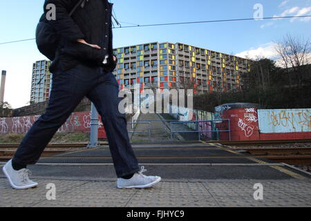 Ein Mann geht durch die Straßenbahnlinien in der Nähe von Park Hill Wohnsiedlung (im Bild) in der Mitte der Stadt von Sheffield, Yorkshire UK Stockfoto