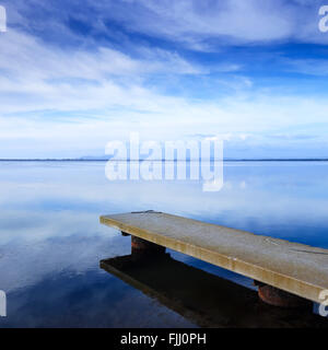 Betonpfeiler oder Steg und am blauen See und bewölkten Himmel Reflexion über Wasser. Stockfoto