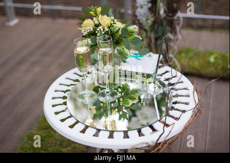 Bouquet und Champagner Gläser auf der Spiegelfläche des Tisches bei einer Trauung im Freien. Stockfoto