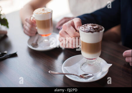 Ein Mann und eine Frau hält eine Tasse Latte Damen- und Herren Hände mit Trauringe mit zwei Tassen Kaffee Stockfoto