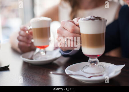 Ein Mann und eine Frau hält eine Tasse Latte Damen- und Herren Hände mit Trauringe mit zwei Tassen Kaffee Stockfoto