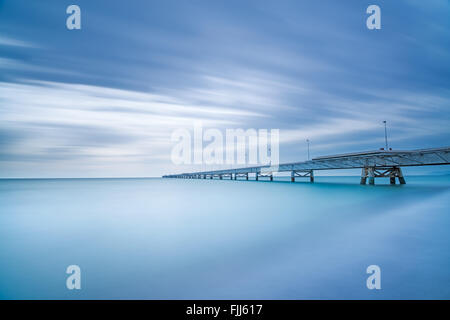 Industrielle Pier auf den Meereshorizont. Seitenansicht. Langzeitbelichtung Fotografie an einem bewölkten Tag. Stockfoto