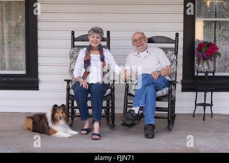 Ein glücklich verheiratetes Paar entspannen Sie auf ihrer Veranda in passende Schwingstühle mit ihrer Sheltie an ihrer Seite. Stockfoto