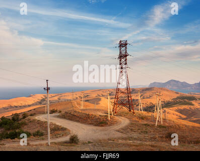 Hochspannungs-Turm in Bergen auf dem Hintergrund der bunten Himmel bei Sonnenuntergang.  Pylon Stromsystem. Sommerabend. Stockfoto