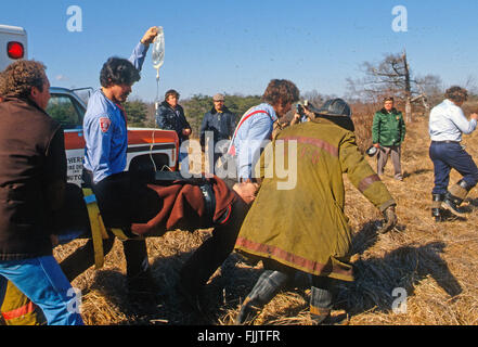 Hyattstown, Maryland, USA, 1978 Montgomery County, Maryland first Responder Ingenieur verletzten Trian von einem entgleisten Zug, der in geraten Brand entfernt haben und tragen ihn zu einem wartenden Maryland State Police Helikopter Flug nach Trauma Center Krankenhaus. Bildnachweis: Mark Reinstein Stockfoto