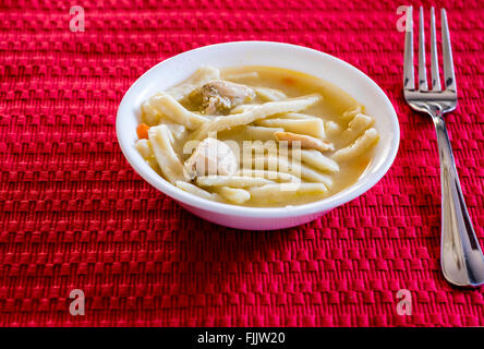 Eine weiße Schüssel voller hausgemachter Hähnchen und Nudeln auf eine rote Platzdeckchen. Oklahoma, USA. Stockfoto