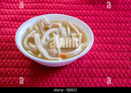 Eine weiße Schüssel voller hausgemachter Hähnchen und Nudeln auf eine rote Platzdeckchen. Oklahoma, USA. Stockfoto