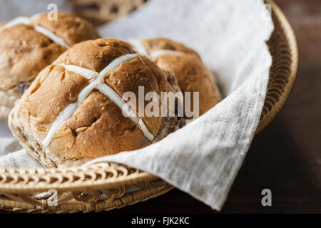 Drei Ostern Hot Cross Buns in einem Korb auf einem rustikalen Holztisch Stockfoto