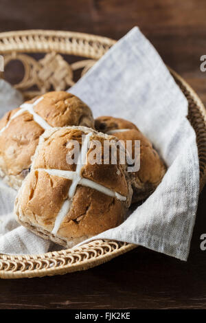 Drei Ostern Hot Cross Buns in einem Korb auf einem rustikalen Holztisch Stockfoto