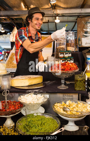 Eine freundliche, lächelnde Essen Anbieter bietet einen Geschmack von Pesto an einem lokalen Markt im Freien in Paris, Frankreich. Stockfoto