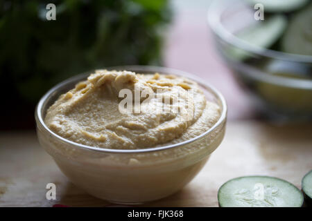 Schüssel mit Hummus auf Tisch mit Gemüse im Hintergrund unscharf. Stockfoto