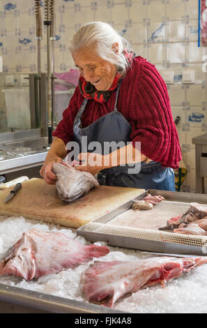 Freundliche alte Frau Fischhändler Reinigung Frischer Fisch in der Vorbereitung für den Verkauf in öffentlichen Markt, Cascais, Portugal Stockfoto