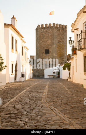Straße mit Kopfsteinpflaster und mittelalterliche Burg Turm in der historischen Stadt Stadt Monsaraz, Alentejo, Portugal Reiseziele Stockfoto