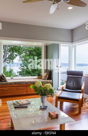 Zeitgenössische gehobene heimische Wohnzimmer mit Leder-Lounge-Sessel, Couchtisch aus Glas, Fensterbank und Fenster mit Blick auf das Wasser Stockfoto