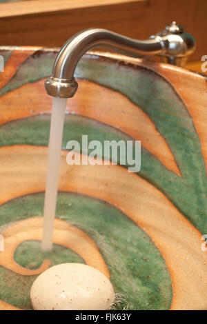 Wasser läuft aus dem Wasserhahn in eine kreative handgefertigte Keramik Waschbecken mit Seife tippen. Abwasch in der kreativen Home bad Interieur. Stockfoto