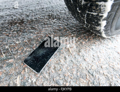 Telefon mit gebrochenen Bildschirm auf Schnee im Auto Trail. Glas bedeckt mit Schneeflocken. Gerät Rad überfahren. Stockfoto