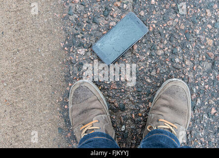 Telefon mit gebrochenen Bildschirm auf Asphalt. Gerät einer Person gelöscht. Stockfoto