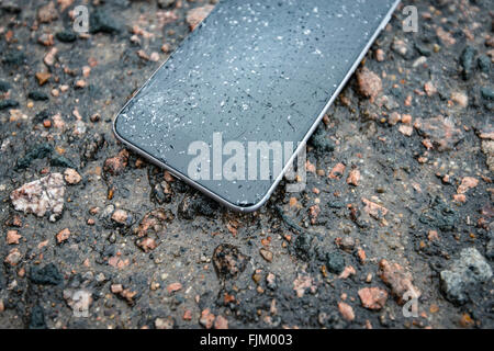 Telefon mit gebrochenen Bildschirm auf Asphalt. Gerät einer Person gelöscht. Glas bedeckt mit Schneeflocken. Stockfoto