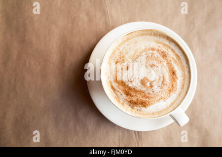 Cappuccino. Tasse Kaffee mit Milchschaum steht über Altpapier auf Tisch in der Cafeteria. Ansicht von oben Stockfoto
