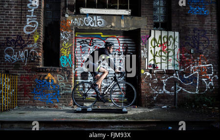 Auf einer Rolle mit Graffiti bemalt Radsportler, Trainer vor einer zerstörten Buling. Stockfoto