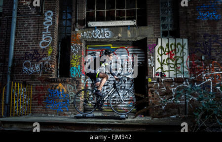 Auf einer Rolle mit Graffiti bemalt Radsportler, Trainer vor einer zerstörten Buling. Stockfoto