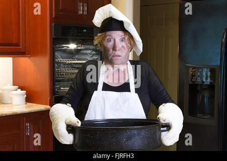 Frau mit Schürze und Köche Hut Holding Bräter mit verkohlten Gesicht. Stockfoto