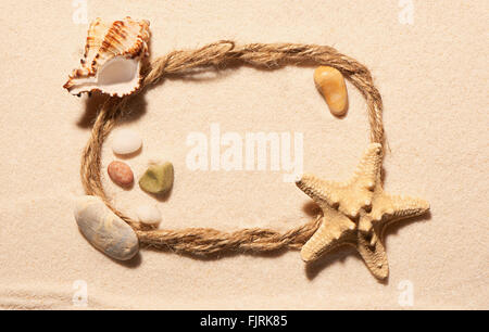 Ovalen Rahmen des Seils mit Seestern, leere Muschel und Steinen auf Sand. Sommer Strand Hintergrund. Ansicht von oben Stockfoto