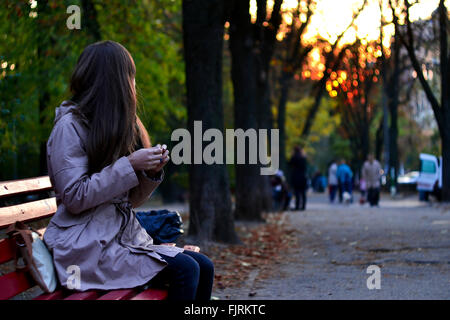 Mädchen sitzen auf der Bank im Park am Abend wartet auf jemanden Stockfoto