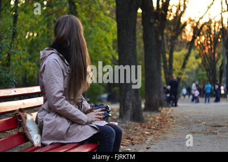 Mädchen sitzen auf der Bank im Park am Abend Stockfoto